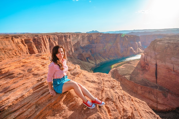 Молодая женщина сидит на краю обрыва с видом на Хорсшу-Бенд в Пейдж, Аризона.