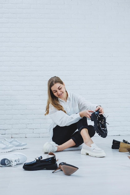 A young woman sits on the floor among shoes and chooses new\
shoes for herself lady in a white shirt and black trousers woman in\
white shoes