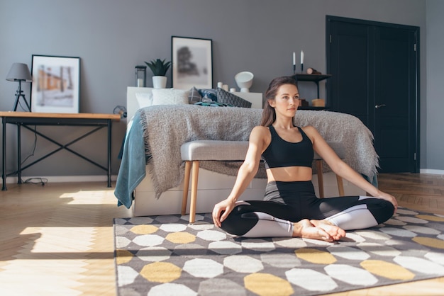 Young woman sits on the floor and presses on her knees stretching the muscles