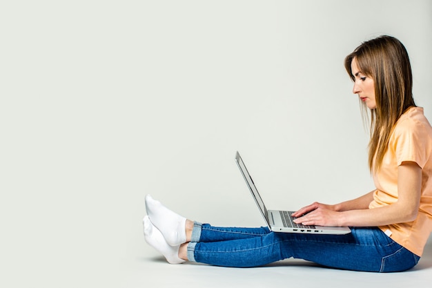 Young woman sits on the floor and works on a laptop on a light space. Banner. Freelance concept, work at home