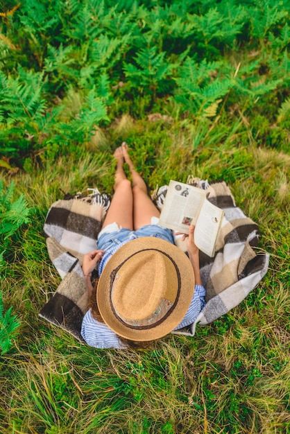 young woman sits on the grass   and reads a book Girl resting on a small picnic near the forest