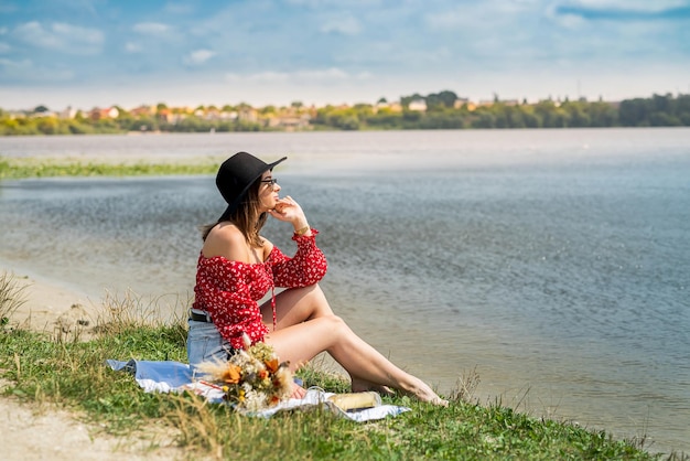 Young woman sits near pond and rest enjoys hot summer day at nature