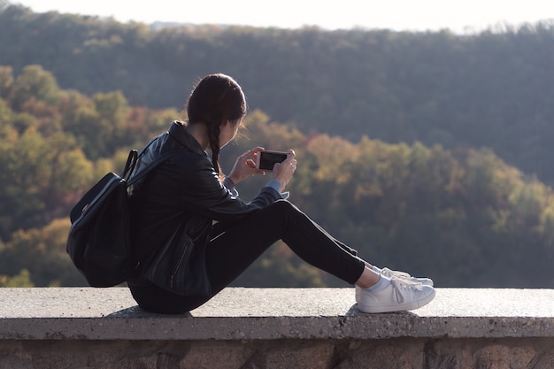 사진 젊은 여자는 자연과 휴대 전화에 사진 만들기에 앉아있다. 스마트 폰의 자연 사진.