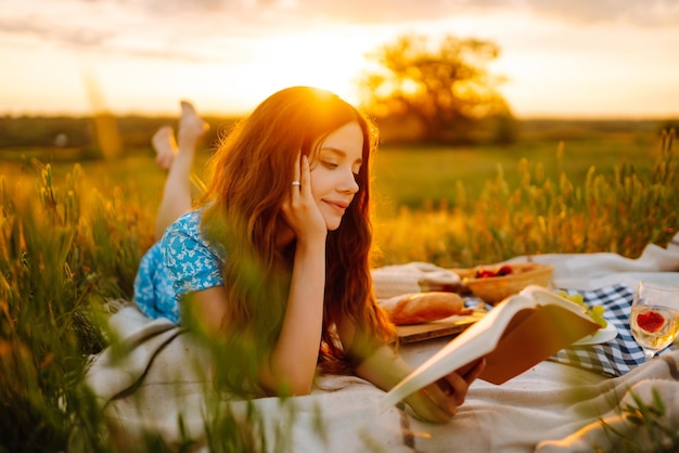 Young woman sits on a plaid with a book Summer picnic in nature Healthy food