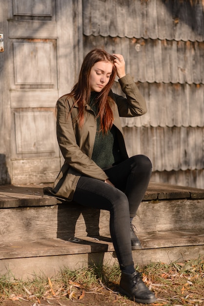 A young woman sits on the steps of a wooden house entrance.