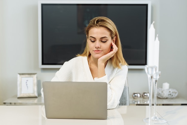 A young woman sits at the table at home and works in a laptop. Businesswoman freelancer.