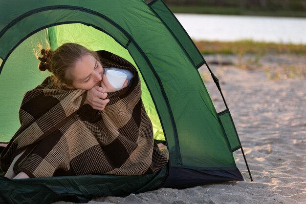 Молодая женщина сидит в туристической палатке, завернутая в одеяло, походы в поход активный туризм