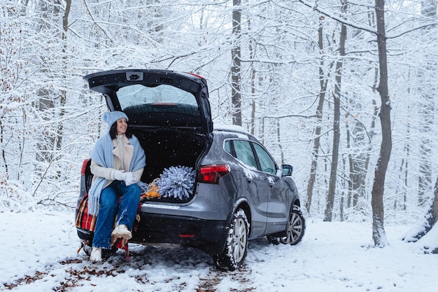 a young woman sits in the trunk of a car in the middle of a winter forest