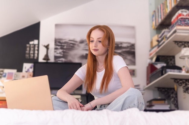 Young woman sits with laptop on bed at home