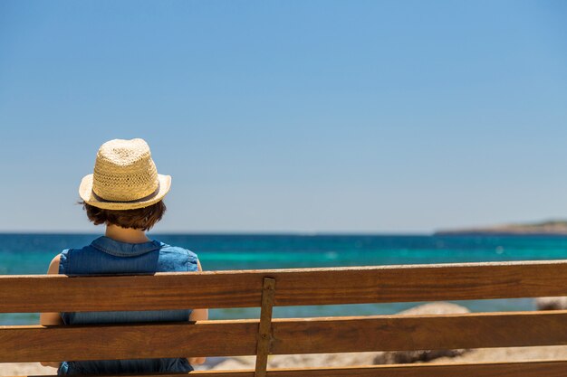 Young woman sitting alone on a bench in front of the sea