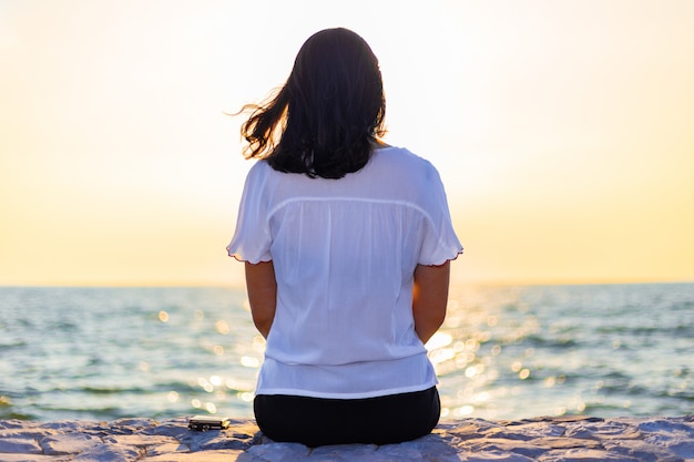 海に沈む夕日を見て一人で座っている若い女性