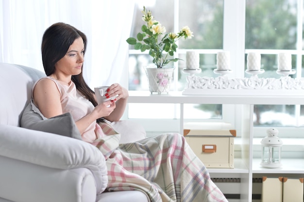 Photo young woman sitting in armchair and drinking tea at light room