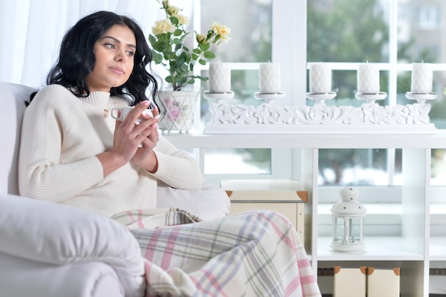 Young woman sitting in armchair and  drinking tea