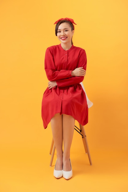 Young woman sitting in armchair on orange background