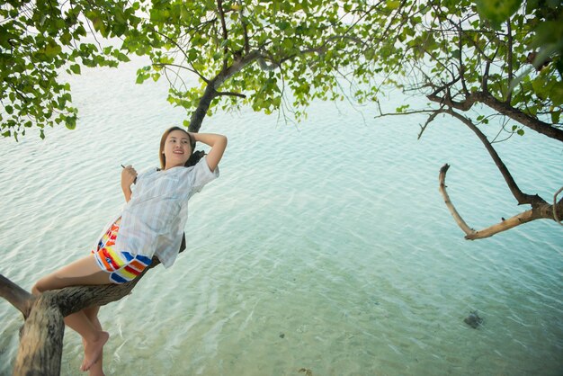 Young woman sitting back on tree with the sea