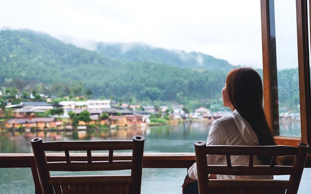 バルコニーに座って、山の村の美しい湖を見ている若い女性