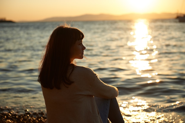 夕暮れ時のビーチに座っていた若い女性