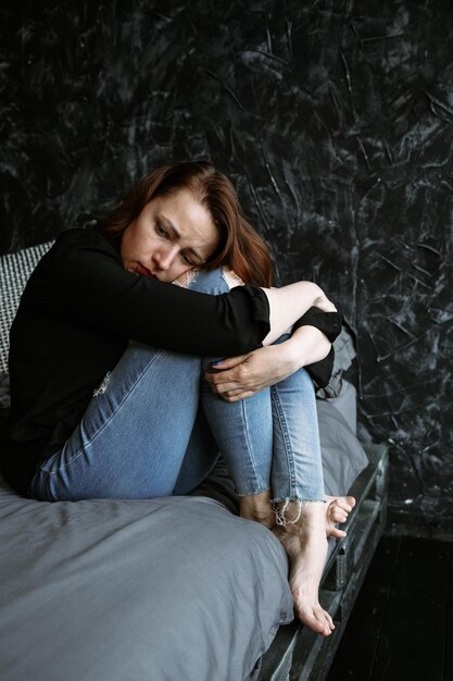 Young woman sitting on bed hugging her knees in pain and\
depression mental health