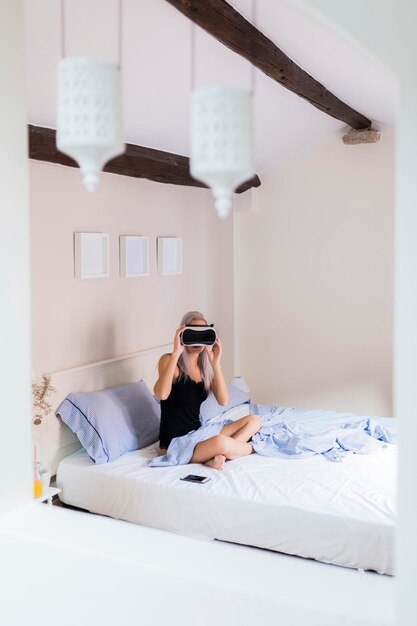 Young woman sitting in bed wearing VR glasses