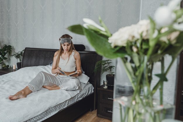 Photo young woman sitting on bed while reading book