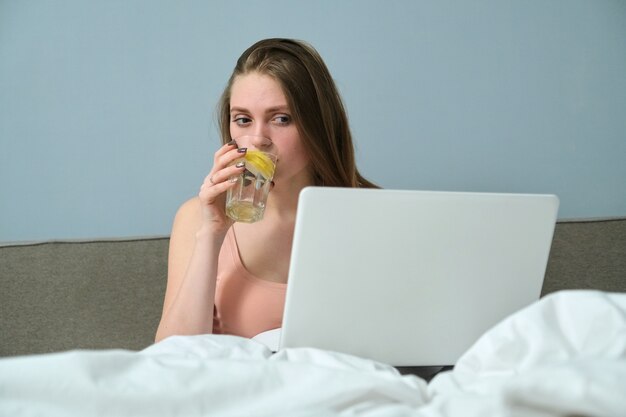 Giovane donna seduta a letto con il computer portatile