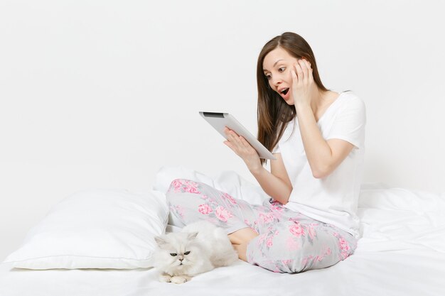 Young woman sitting in bed with white cute Persian silver chinchilla cat isolated on white wall