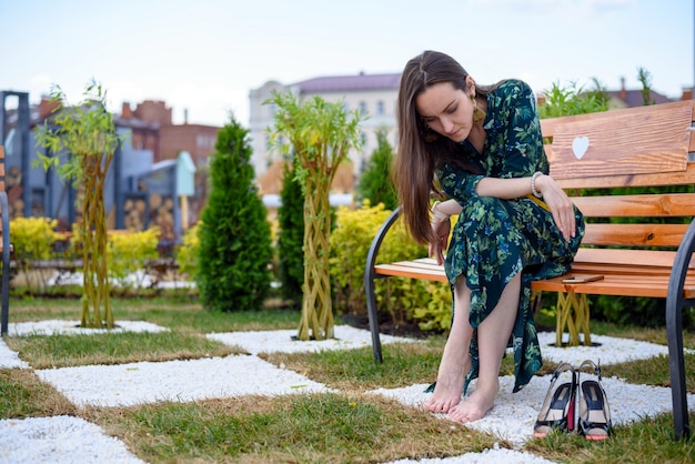 Young woman sitting on bench barefoot next to high heel shoes