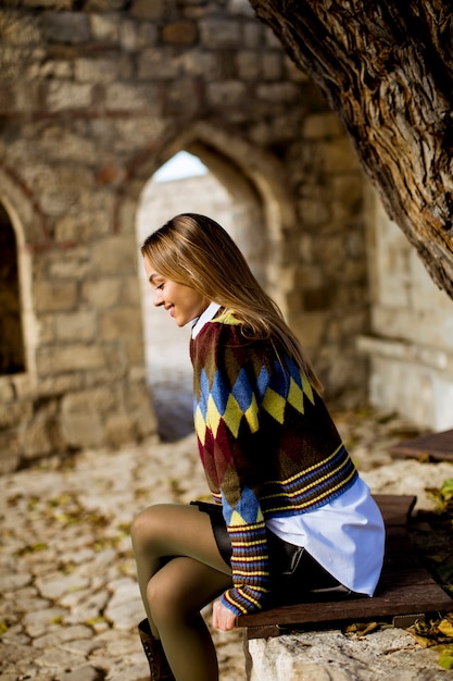 Young woman sitting on the bench watching yellow leaves tree in the autumn park