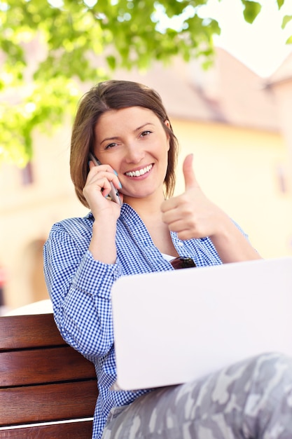 Photo young woman sitting on bench with computer