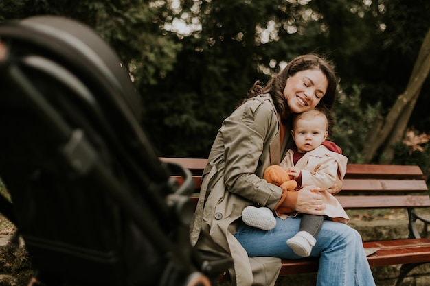 Young woman sitting on a bench with a cute baby girl in the autumn park