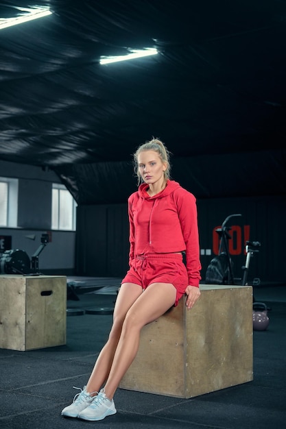 Young woman sitting on a box at gym after her workout and looking at the camera