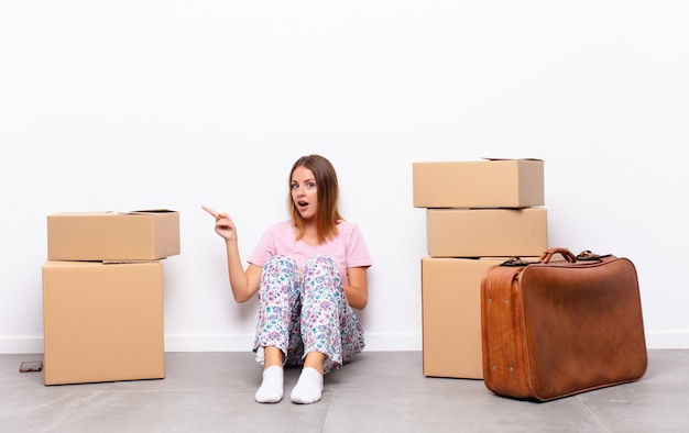 young woman sitting between boxes pointing amazed to the side