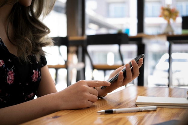 Giovane donna seduta in una caffetteria luminosa e utilizzando smart phone