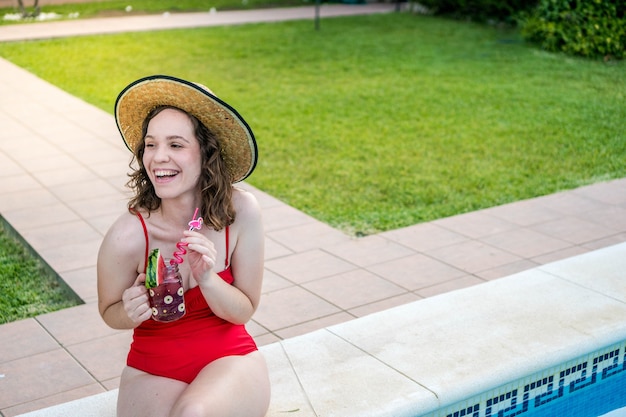 プールのそばに座って赤い水着を着ている若い女性夏にカクテルを飲む女性