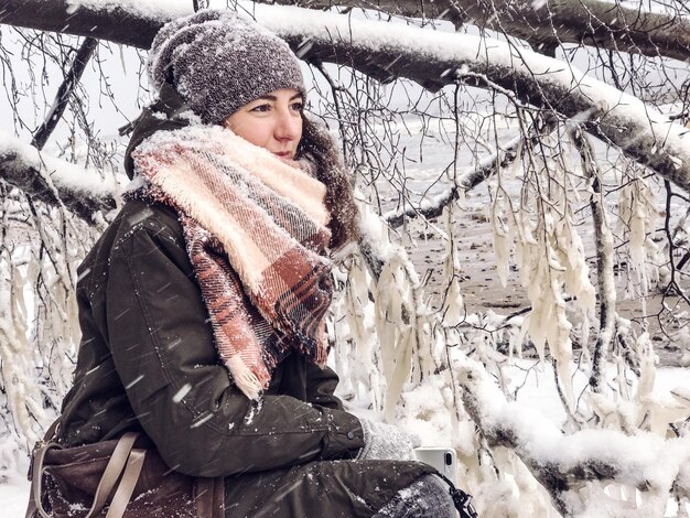 写真 野原で雪で覆われた裸の木のそばに座っている若い女性