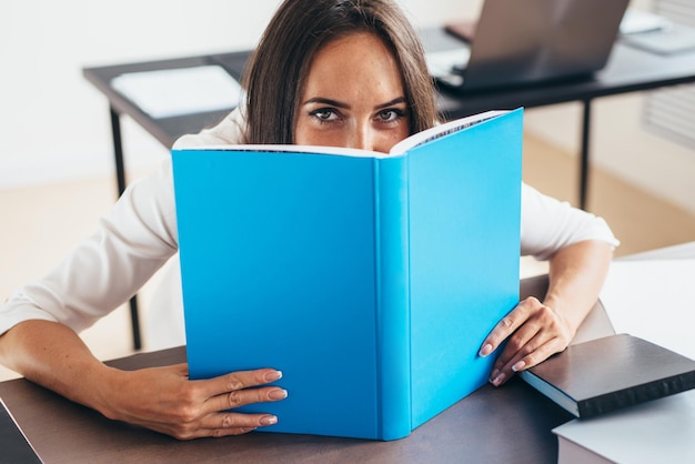 Young woman sitting by table and reading book