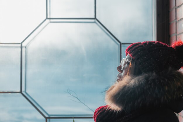 Young woman sitting by the window and looking at frozen glass. 