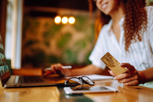 Молодая женщина сидит в кафе и делает покупки в Интернете с помощью кредитной карты и ноутбука