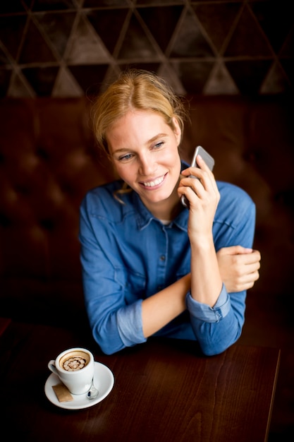 Young woman sitting in cafe, using telephone and drinking coffe