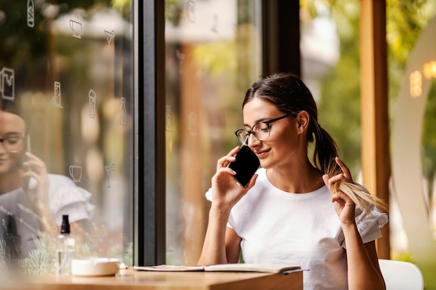 A young woman sitting in a cafeteria looking at the menu and talking on the phone