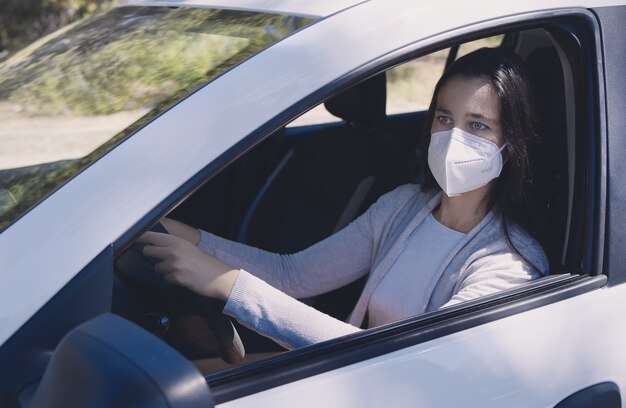 Young woman sitting in a car wearing a protective mask during the COVID-19 pandemic