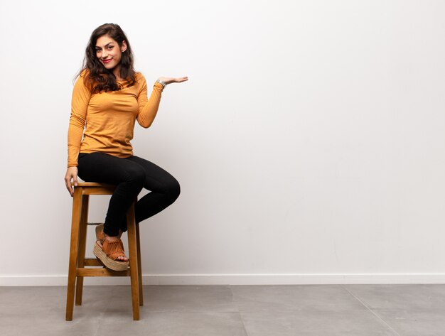 young woman sitting on a chair next to copyspace, presenting a product