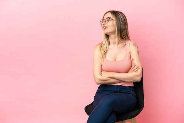 Young woman sitting on a chair over isolated pink background happy and smiling