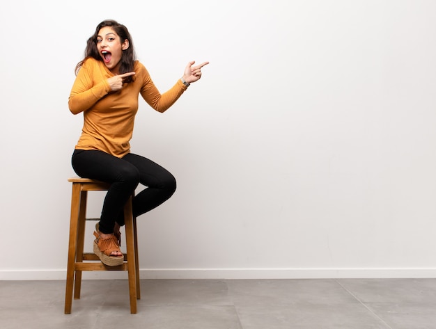 young woman sitting on a chair pointing at copyspace