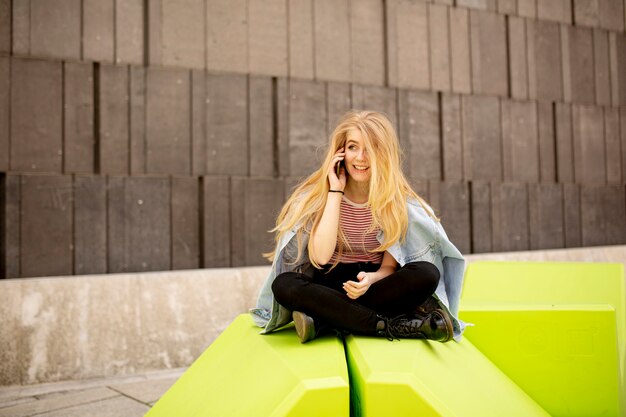 Young woman sitting in the city and use a mobile phone. Urban concept.