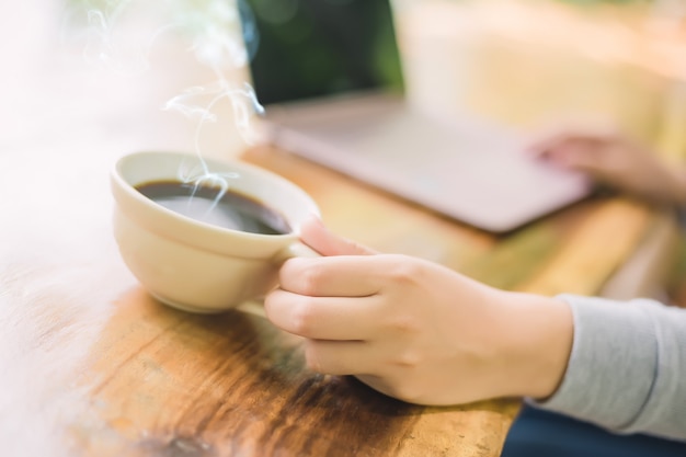 Young woman sitting in coffee shop at wooden table, drinking coffee and using laptop.