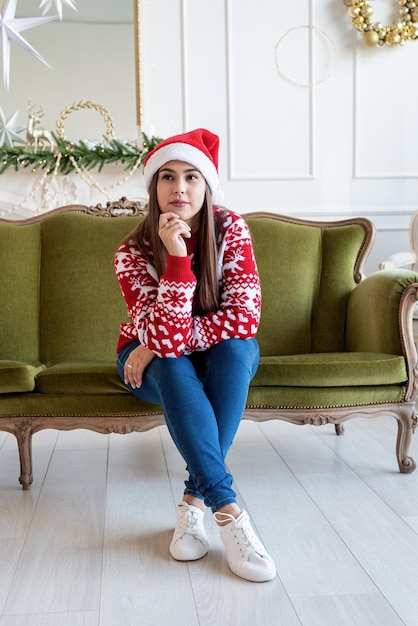 Молодая женщина сидит на диване одна в украшенной на Рождество гостиной