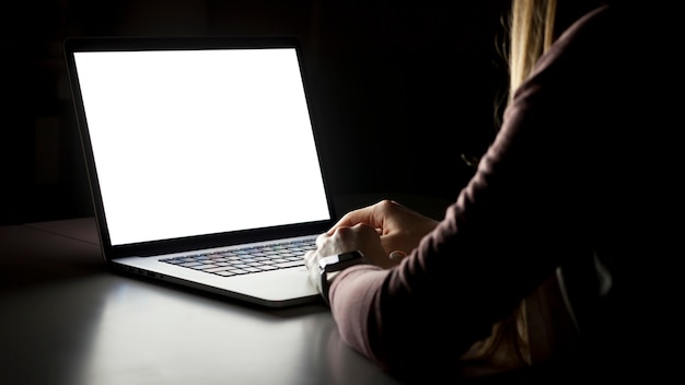 Young woman sitting in the dark living room and working on laptop