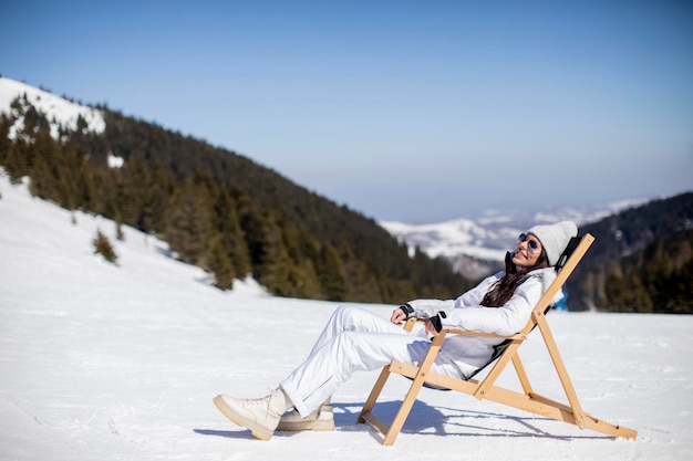 Молодая женщина сидит в шезлонге на лыжной трассе у заснеженной горы