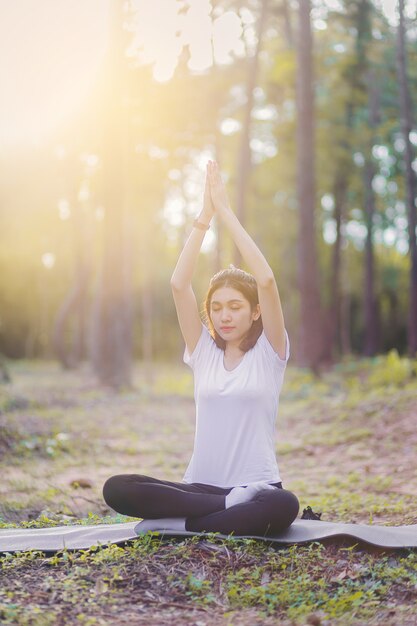 Giovane donna che si siede e che fa posa di yoga con priorità bassa della foresta e dell'alba.
